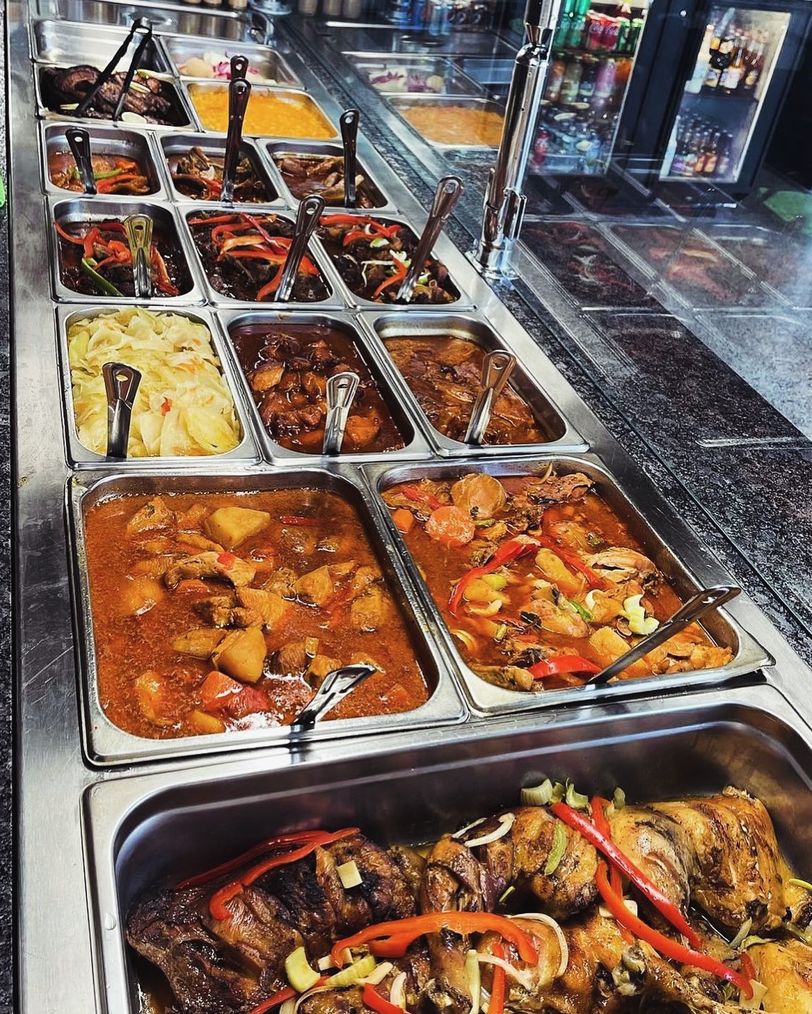 Caribe steam table loaded with stews, curries, cabbage, and roasted meats