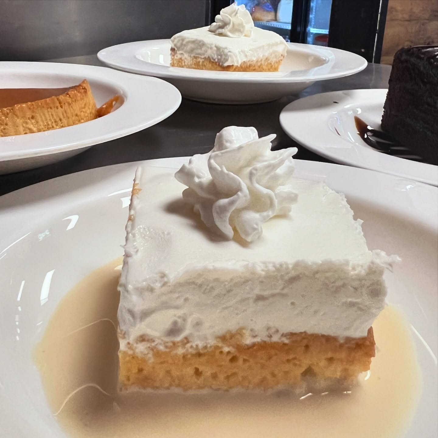 Slice of tres leches with whipped cream swirl in a pool of sweet milk