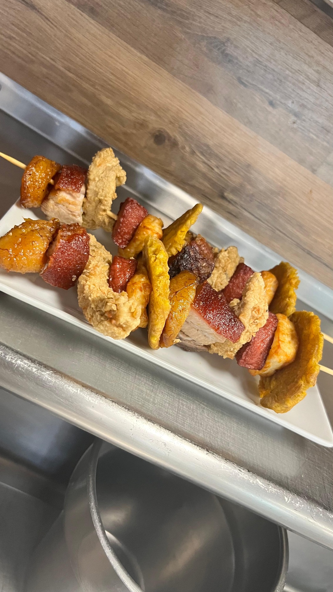 Pinchos skewers of pork belly, chicken, and sweet plantain on a white plate