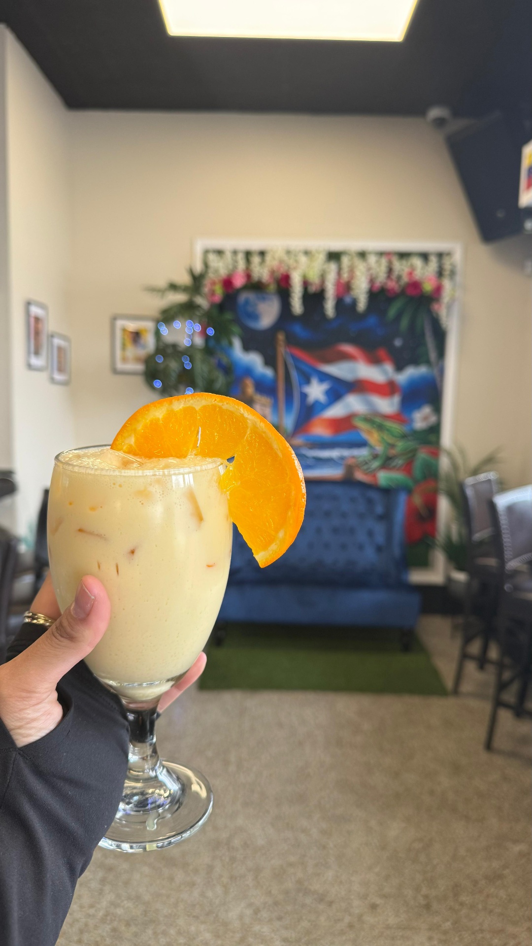 Creamy coquito cocktail garnished with an orange slice in front of the Caribe Puerto Rico mural