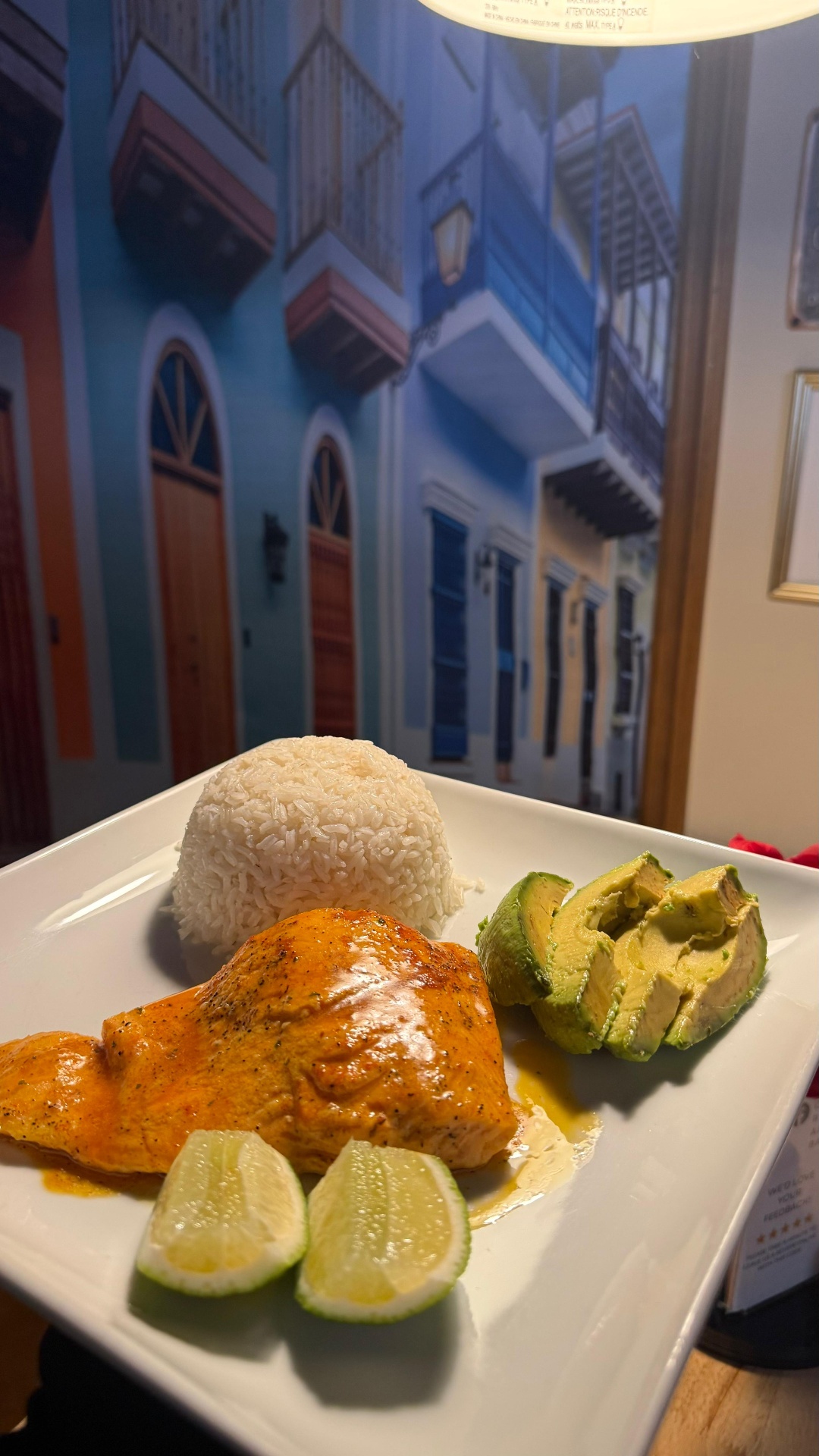 Plate of seared salmon with white rice, avocado, and lime in front of an Old San Juan mural